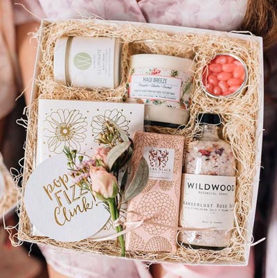 กล่องของขวัญ Wedding Gift Box โทนสีชมพูพาสเทลและขาว บรรจุเทียนหอม กลิ่น Maui Breeze, เกลือสปา Wildwood, ครีมทาผิว, ขนม และการ์ดอวยพร ตกแต่งด้วยดอกไม้สดบนฟางไม้แห้ง